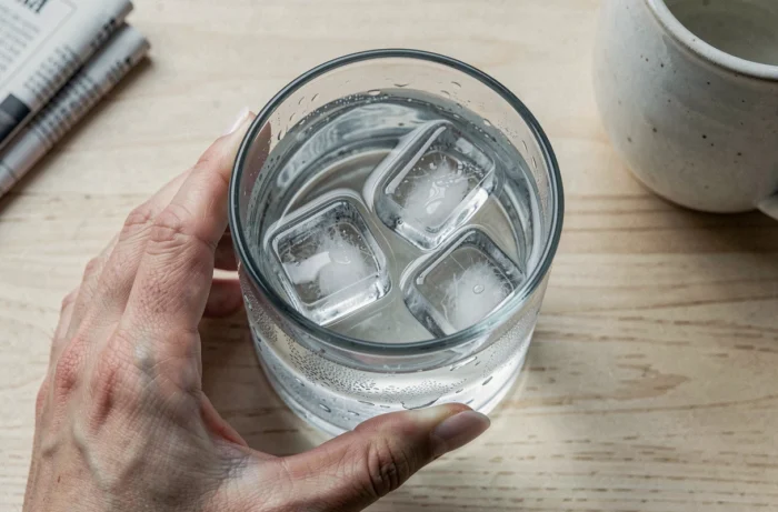Vue aérienne rapprochée d'un verre d'eau avec des glaçons posé sur une table en bois, gouttelettes de condensation visibles, évoquant l'importance de l'hydratation et des signaux de santé quotidiens