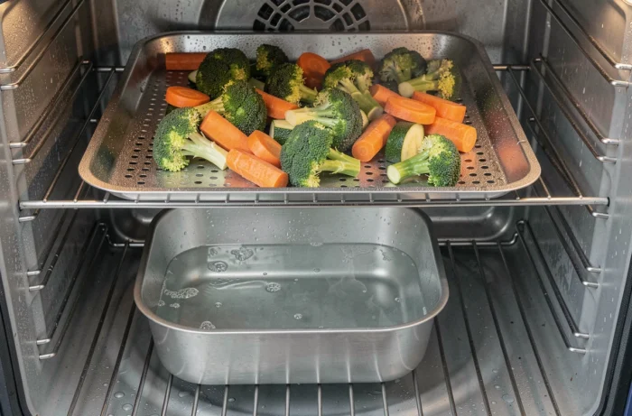 Vue intérieure d'un four avec bac d'eau et grille de légumes vapeur, gouttelettes de condensation visibles sur les parois